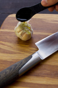 pouring olive oil on garlic bulb before roasting for vegan cauliflower mashed potatoes with mushroom gravy