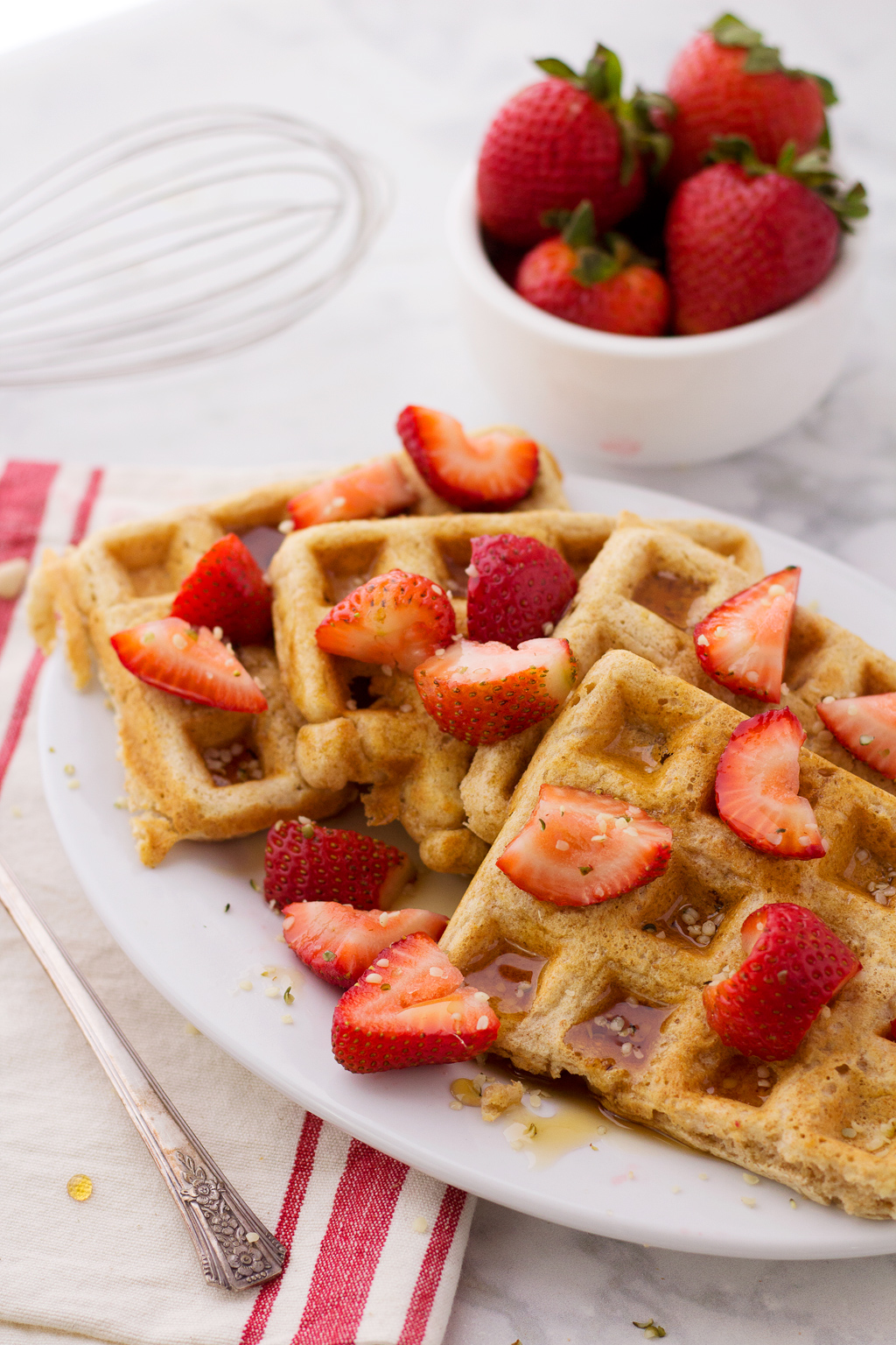 Finished vegan waffles topped with maple syrup, hemp seeds, and strawberries