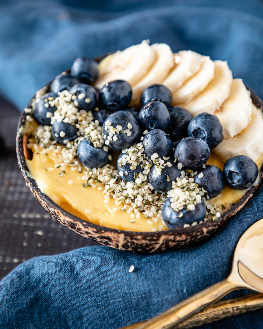Copycat dole whip smoothie bowl filled in coconut bowl, topped with banana and blueberry