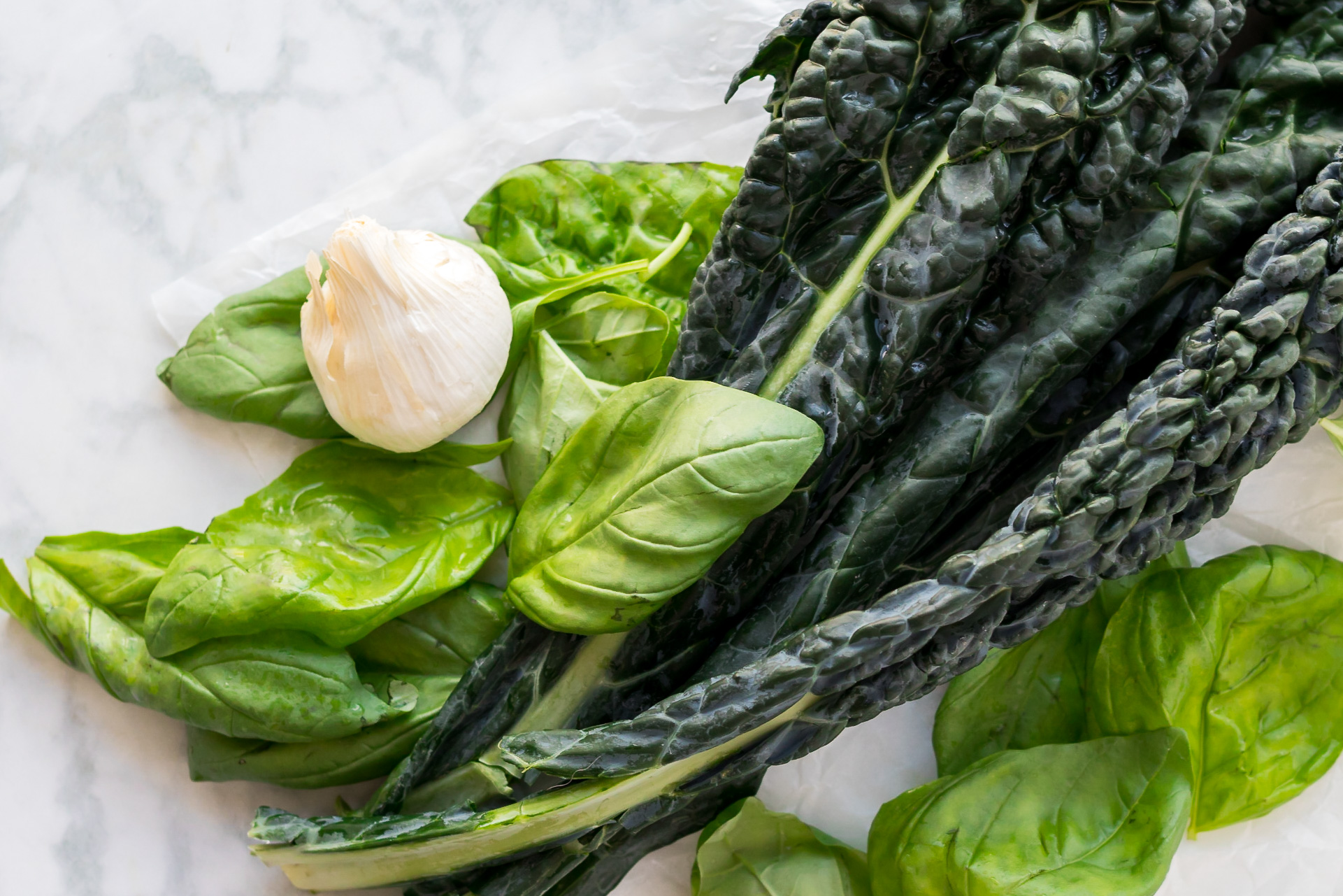 Garlic, basil, and kale on marble representing whole foods vegan multivitamins